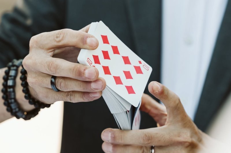 Un homme en costume manipule un jeu de cartes, mettant en avant une carte de carreau rouge.