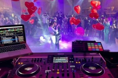 Vue d'une table de mixage de DJ avec un couple dansant au centre d'une salle décorée de ballons rouges en forme de cœur.
