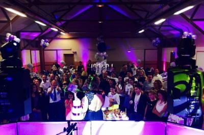 Un groupe de personnes rassemblées dans une salle décorée, éclairée par des lumières colorées, lors d'un événement festif.