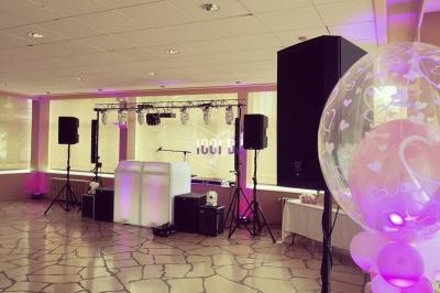 Salle décorée pour un événement avec éclairage rose, piste de danse, enceintes et ballon transparent à motifs de cœurs.