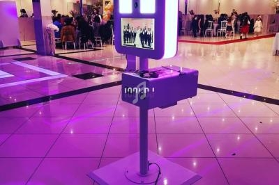 Borne photo interactive éclairée en rose dans une salle de réception avec des invités en arrière-plan.