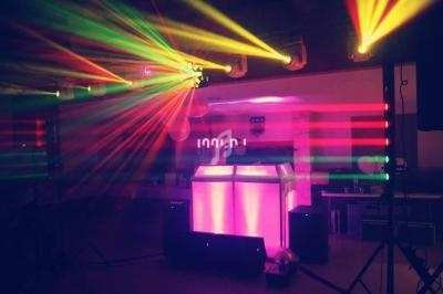 Jeu de lumières colorées projetées autour d'une console de DJ éclairée dans une salle sombre.