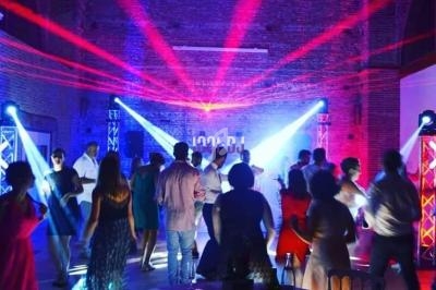 Des personnes dansent sous des lumières colorées dans une salle en briques, ambiance festive et animée.