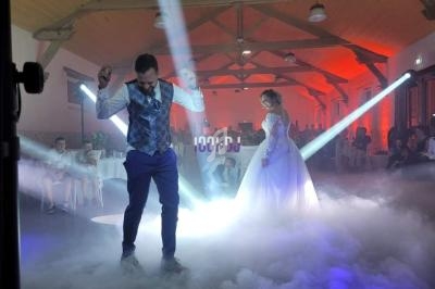Un couple danse sur une piste éclairée par des projecteurs, entourée de fumée dans une salle de réception.