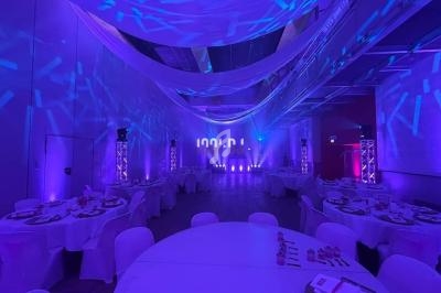 Salle de réception décorée avec des tables rondes, éclairage violet et drapés suspendus au plafond.