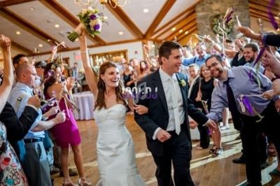 Un couple de mariés souriants marche au milieu d'invités célébrant avec des rubans dans une salle lumineuse.