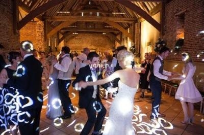 Des invités dansent dans une salle en bois et briques, éclairée par des jeux de lumière.