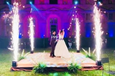 Un couple danse sous des fontaines d'étincelles sur une scène extérieure illuminée devant un bâtiment éclairé.