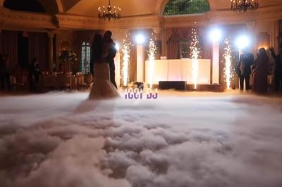 Un couple danse sur une piste entourée d'effets de fumée et d'étincelles dans une salle de réception élégante.