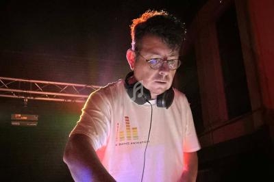 Un DJ portant un casque audio mixe de la musique sur une scène éclairée par des lumières colorées.