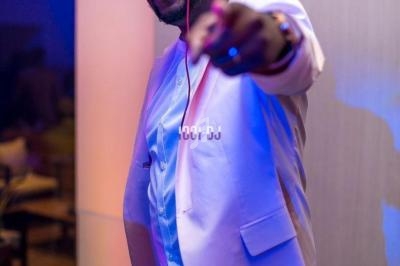 Un DJ souriant en costume clair mixe de la musique dans une ambiance lumineuse et festive.