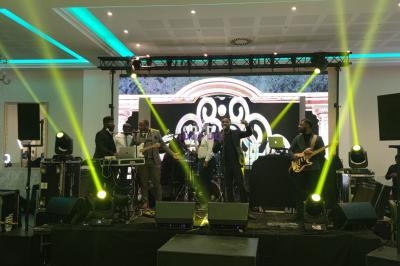 Un groupe de musiciens et chanteurs se produit sur une scène éclairée par des projecteurs dans une salle de réception.