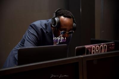 Un DJ portant un casque audio se penche sur des équipements derrière un ordinateur dans une ambiance sombre.