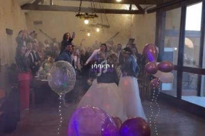 Un couple de mariés danse devant des invités dans une salle décorée de ballons et de lanternes suspendues.