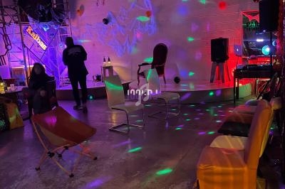 Salle avec éclairage coloré, chaises disposées, décor industriel et ambiance festive.