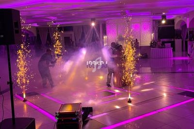 Un couple danse au centre d'une salle illuminée de lumières violettes, entouré d'effets pyrotechniques et de fumée.