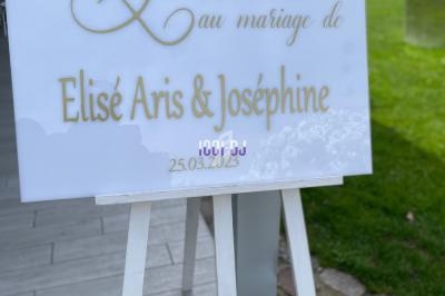 Panneau blanc sur chevalet indiquant ’Bienvenue au mariage de Élise Aris & Joséphine, 25.03.2023’, placé en extérieur.