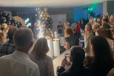 Groupe de personnes réunies dans une salle, regardant un gâteau avec des cierges allumés lors d'une célébration.