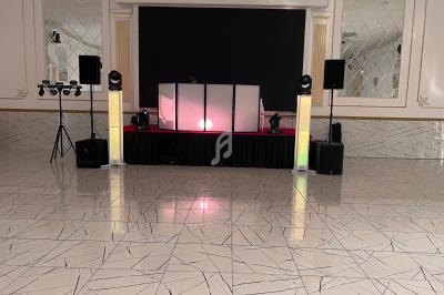 Salle de réception avec sol en marbre, scène équipée d'un DJ, éclairages et enceintes.