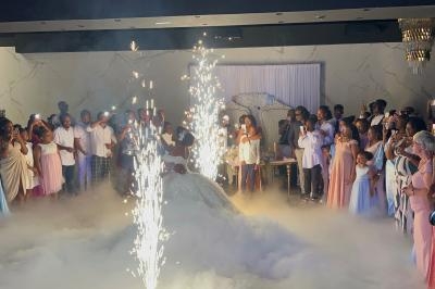 Un couple danse au centre d'une salle entourée d'invités, avec des étincelles et de la fumée au sol.