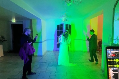 Un couple danse sous des lumières colorées tandis que des invités les observent et prennent des photos.