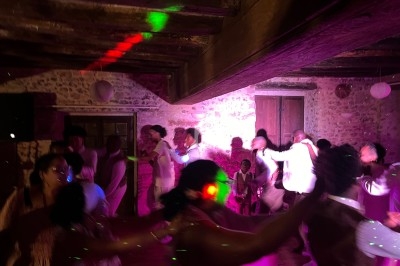Des personnes dansent dans une salle en pierre éclairée par des lumières colorées, créant une ambiance festive.