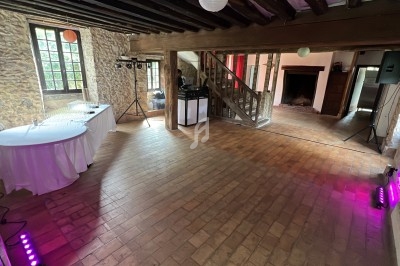 Salle en pierre avec parquet, éclairage coloré, table ronde dressée et équipement audio près d'un escalier en bois.