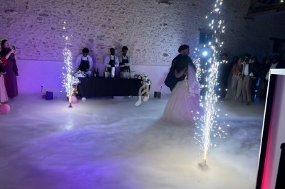 Un couple danse dans une salle éclairée, entouré de fumée au sol et de fontaines d'étincelles.