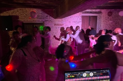 Personnes dansant en groupe dans une salle en pierre éclairée par des lumières colorées, avec une table de mixage au premier…