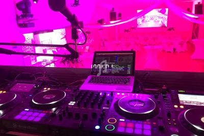 Poste de DJ avec platines, table de mixage et ordinateur, dans une salle décorée de lumières roses pour un événement.