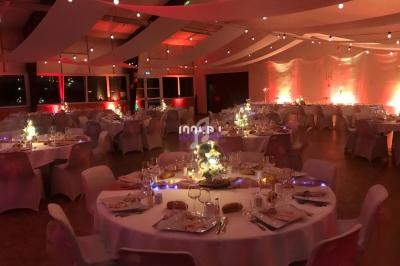Salle de réception décorée avec des tables rondes dressées, éclairage tamisé et ambiance chaleureuse.