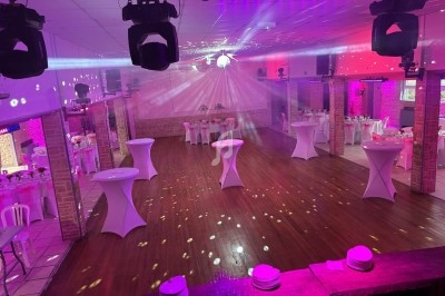Salle de réception décorée avec des tables hautes et des jeux de lumière, prête pour un événement festif.