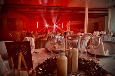 Salle de réception décorée avec des tables dressées, bougies et guirlandes, éclairée par des lumières rouges.