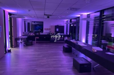 Salle moderne avec éclairage violet, tables alignées, matériel audio et baies vitrées donnant sur un extérieur nocturne.