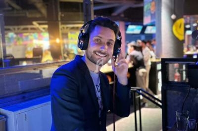 Homme souriant portant un casque audio, debout dans un environnement lumineux avec des personnes en arrière-plan.