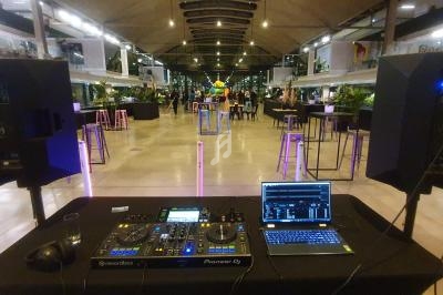 Table de mixage DJ avec ordinateur portable et haut-parleurs dans une salle moderne éclairée, prête pour un événement.
