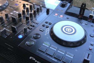 Table de mixage DJ avec platine, boutons et commandes, posée sur une surface perforée en extérieur.