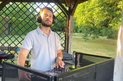 Un DJ mixant de la musique en extérieur sous un kiosque en bois, entouré de verdure.