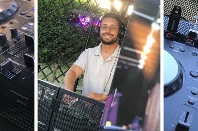 Un homme souriant se tient derrière une table de mixage avec des équipements DJ, en extérieur.
