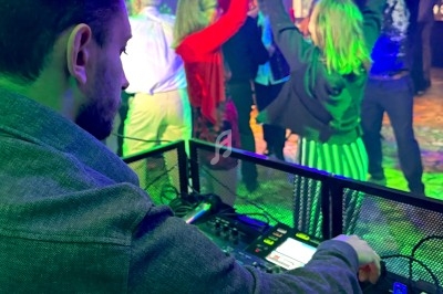 Un DJ mixe de la musique tandis que des personnes dansent sous des lumières colorées dans une salle festive.