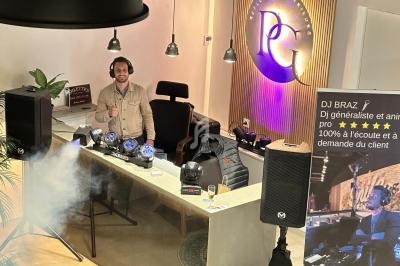 Un DJ derrière une table de mixage avec éclairage et matériel audio, dans un espace moderne avec un panneau lumineux.