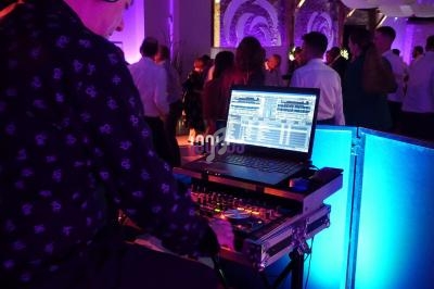 Un DJ mixe de la musique sur une console avec un ordinateur portable, lors d'une soirée dansante éclairée par des lumières…