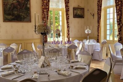 Salle de réception élégante avec tables rondes dressées, nappes blanches et décorations florales, éclairée par la lumière…