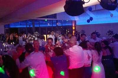 Des invités dansent en cercle dans une salle décorée pour une fête, éclairée par des lumières colorées.