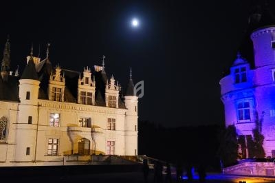 Château éclairé de nuit sous une pleine lune, avec une tour illuminée en bleu et des silhouettes de visiteurs.