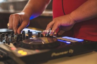 Mains ajustant les commandes d'une table de mixage DJ avec des lumières colorées en arrière-plan.