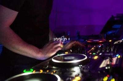 Un DJ mixe de la musique sur une table de mixage éclairée par des lumières violettes dans une ambiance sombre.