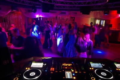 Vue depuis une table de mixage sur une piste de danse animée, éclairée par des lumières colorées dans une salle festive.