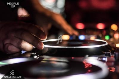 Main posée sur une platine de DJ en pleine utilisation, avec des lumières floues en arrière-plan.