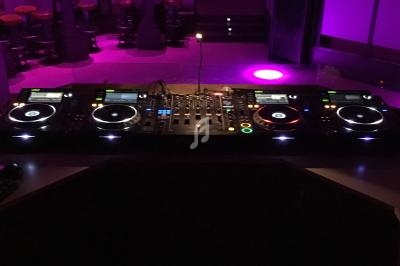 Table de mixage professionnelle avec plusieurs platines, écrans et ordinateurs dans un environnement éclairé en violet.